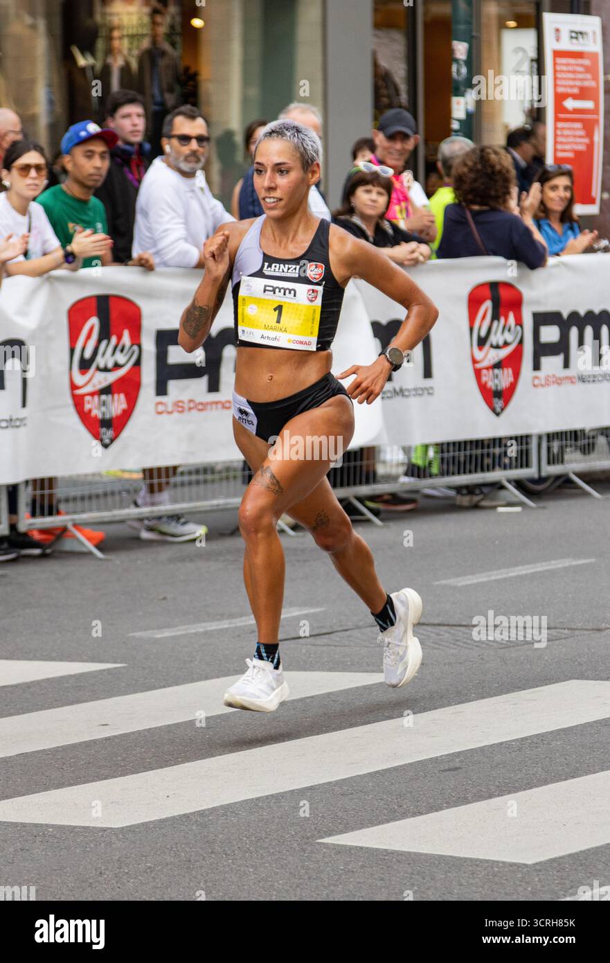 Marathonläuferin bewegt sich kraftvoll durch die Stadtstraße mit farbenfrohen Gebäuden, während begeisterte Zuschauer ihre Fitness feiern Stockfoto
