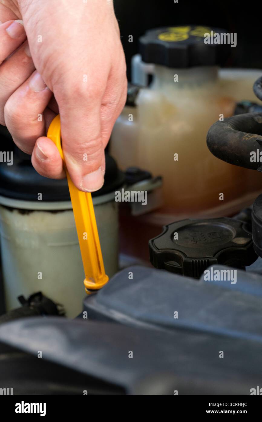 Nahaufnahme einer Person, die einen gelben Ölmessstab aus einem Fahrzeugmotor herauszieht, um den Ölstand zu prüfen. Nützlich für Wartungs- und Reparaturanleitungen für Kraftfahrzeuge Stockfoto