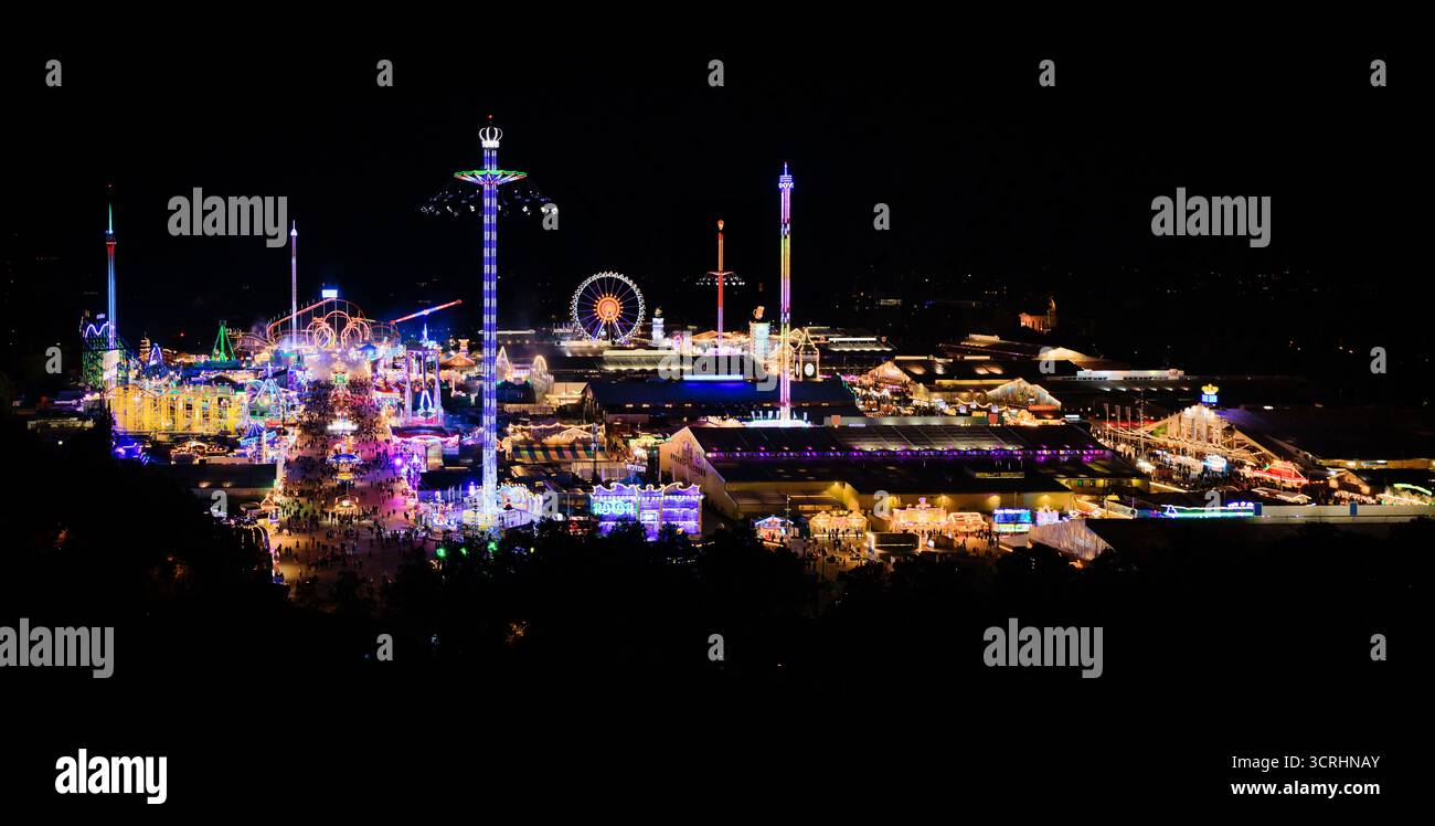 Panorama des Oktoberfestes in München bei Nacht - weltberühmtes Volksfest mit farbenfroher Beleuchtung, Fahrgeschäften und gemütlichen Zelten in bayerischer Metropole - Keim Stockfoto