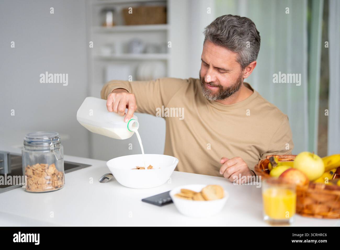 Mann 40 isst in der Küche. Der Kerl genießt morgens frisches Essen am Küchentisch. Ein Mann isst Getreide und Obst in der Küche. Mann Stockfoto
