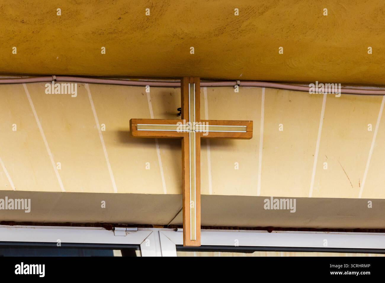 Holzkreuzschild an der beigefarbenen Ladenfront-Wand mit modernem Intarsien-Design für Kirche oder Geschäft Stockfoto