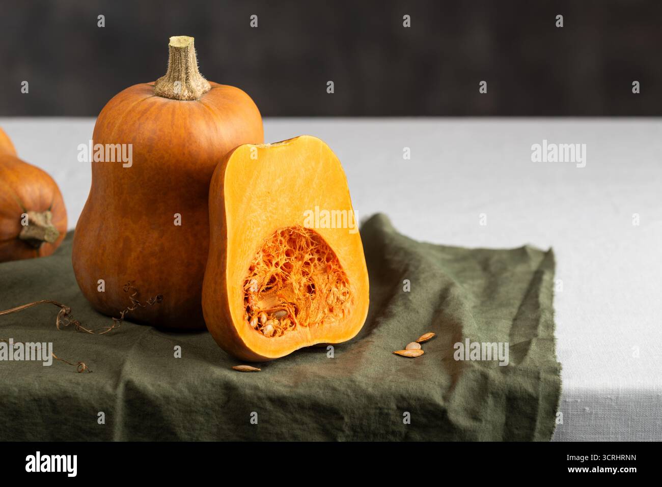 Honeynut Squash Slice mit Samen und leuchtendem Orangenfleisch, das neben ganzen Mini Butternut Kürbissen auf Einem Küchentisch liegt Stockfoto