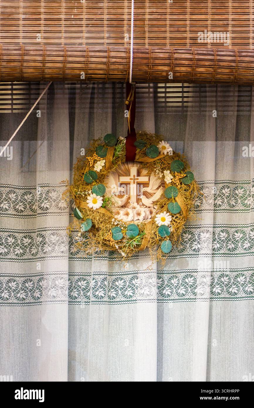 Rustikaler Blumenkranz mit Kreuz, Daisies und Grün auf Spitzenvorhang im Wohnkultur-Stil Stockfoto