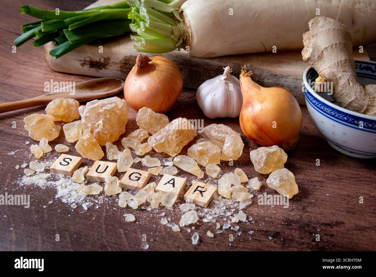 Steinzucker in verschiedenen Formen und Größen auf einer Küchenarbeitsfläche zusammen mit verschiedenen Gemüse zum Kochen. Stockfoto