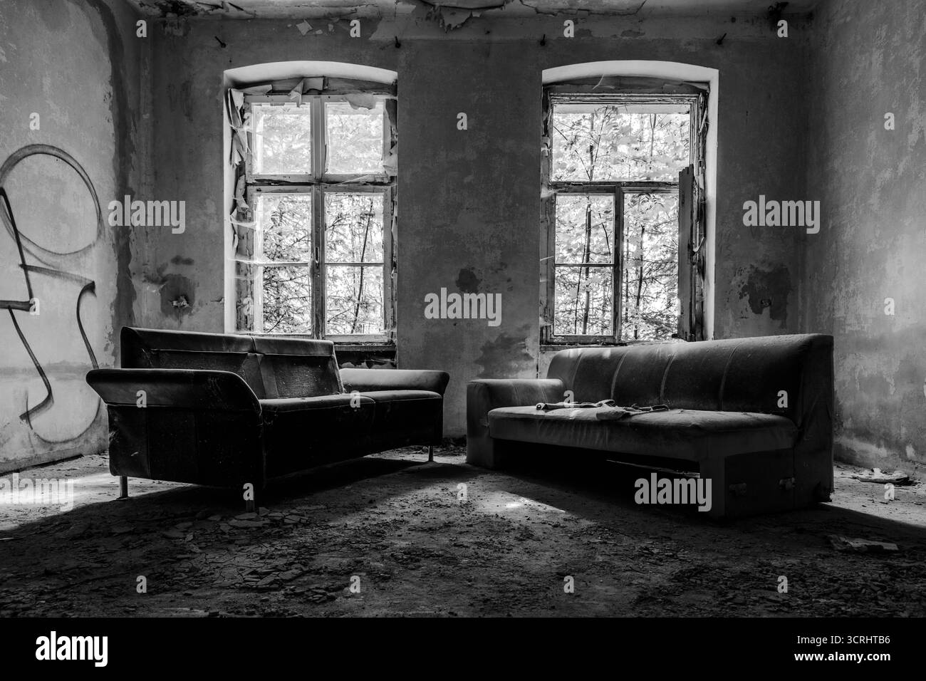 Verlassenes Zimmer mit Vintage-Sessel und Sofa in der Nähe eines kaputten Fensters, Stadtfotografie mit natürlichem Licht Stockfoto