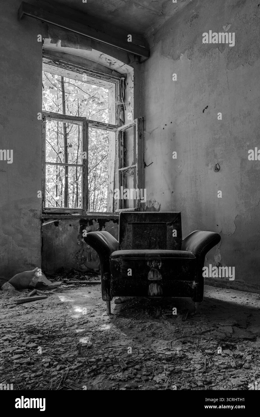 Verlassenes Zimmer mit Vintage-Sessel und Sofa in der Nähe eines kaputten Fensters, Stadtfotografie mit natürlichem Licht Stockfoto