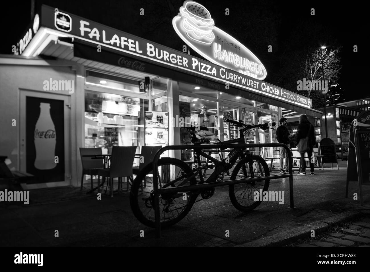 Nächtliche Straßenszene mit Fahrrad und beleuchtetem Fast-Food-Stand, Urban Lifestyle und City Nightlife in Schwarz und weiß Stockfoto