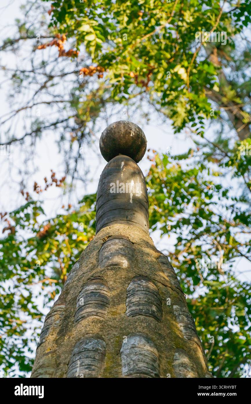 Nahaufnahme einer Steinstruktur mit kugelförmiger Spitze, umgeben von grünen Blättern und Sonnenlicht, die Harmonie von Architektur, Natur und einfangen Stockfoto