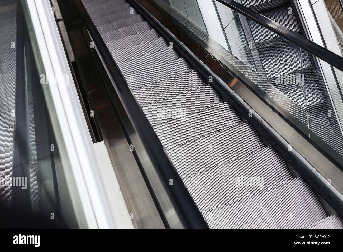 Leere, moderne Rolltreppe im Innern des Einkaufszentrums. Metallstufen und Glasgeländer mit Reflexionen. Städtische Architektur und Verkehrskonzept. Stockfoto