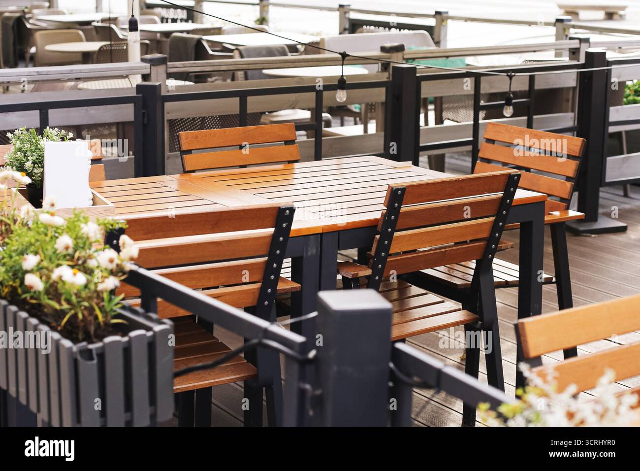 Außenterrasse mit Holztischen. Sitzbereich im Restaurant mit Stühlen. Gemütlicher Speisesaal im Sonnenlicht. Moderne Möbel für Gastfreundschaft Service. Stockfoto