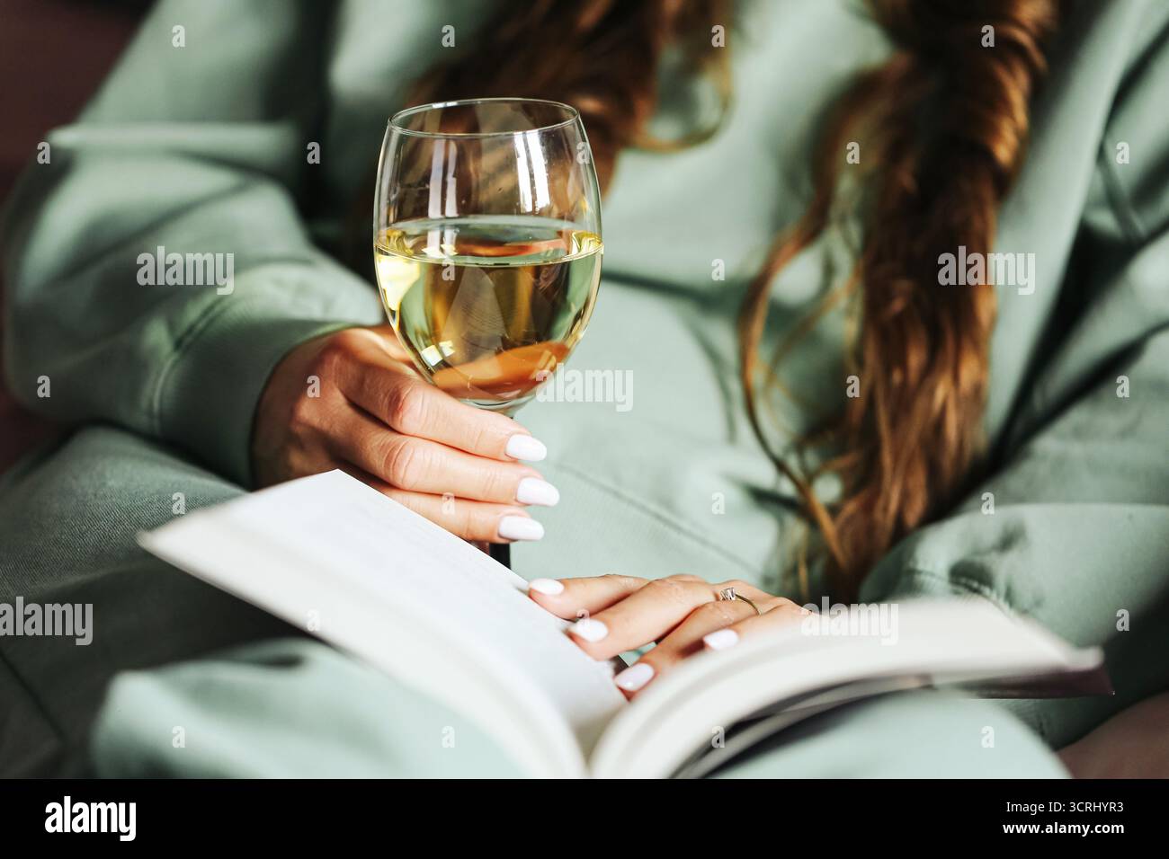 Frau mit einem Glas Weißwein, das Buch liest. Entspannende Freizeit zu Hause. Gemütlicher Lifestyle-Moment mit Drink und Literatur. Ruhige Atmosphäre. Stockfoto