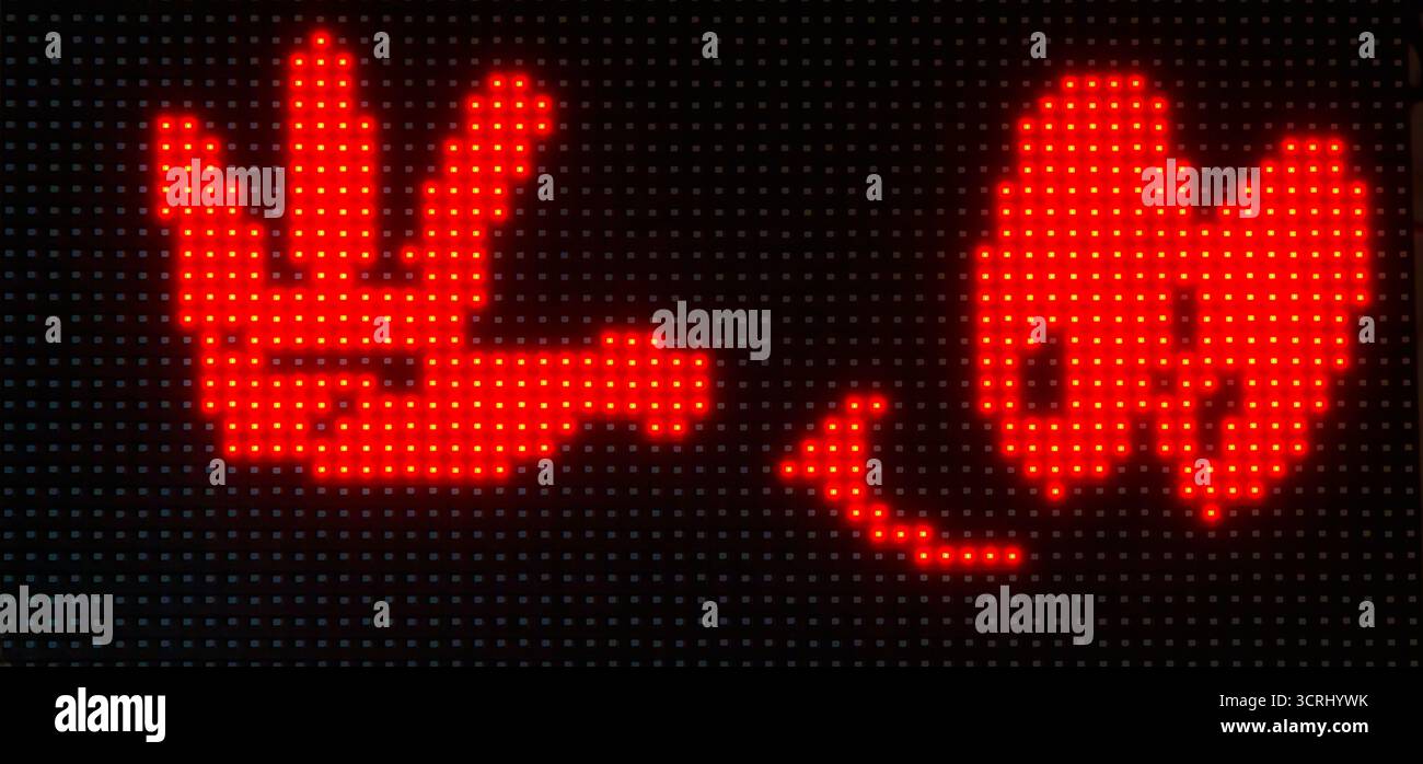 Nahaufnahme eines leuchtend roten LED-Lichtdisplays, das eine spielerische Handbewegung und ein lächelndes Gesicht zeigt, aufgenommen bei Nacht vor einem schwarzen digitalen Bildschirm Stockfoto