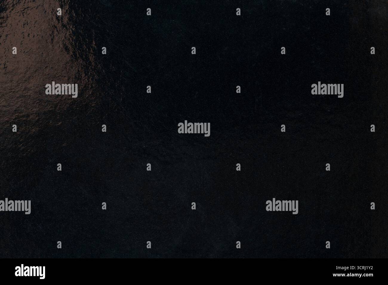 Glatte, schwarze reflektierende Oberfläche fängt Licht ein und zeigt Textur und Tiefe bei weicher Umgebungsbeleuchtung. Stockfoto