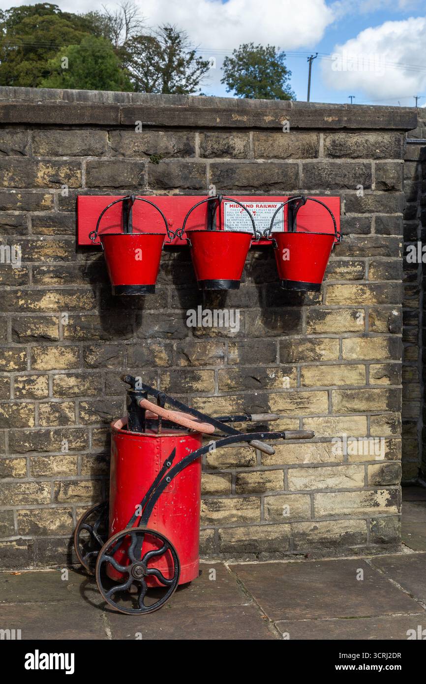 Historische rote Feuereimer und ein roter Wagen voller Ausrüstung an der Oakworth Station, Teil der Keighley and Worth Valley Railway in Yorkshire. Stockfoto