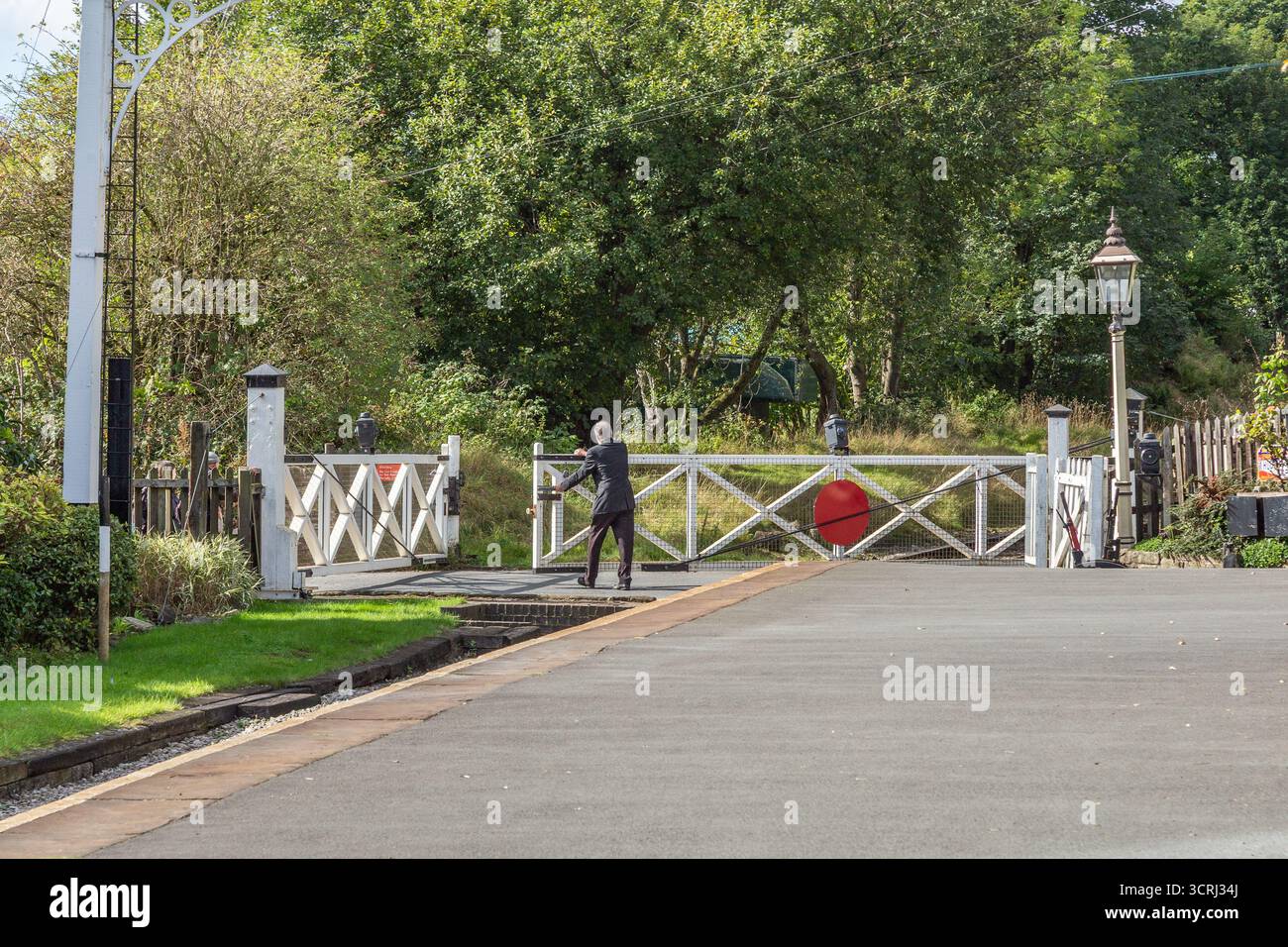 Ein Bahnhofsmeister schließt das Tor an einem Bahnübergang an der Oakworth Station, Yorkshire. Der Bahnhof befindet sich an der Keighley and Worth Valley Dampfeisenbahn. Stockfoto