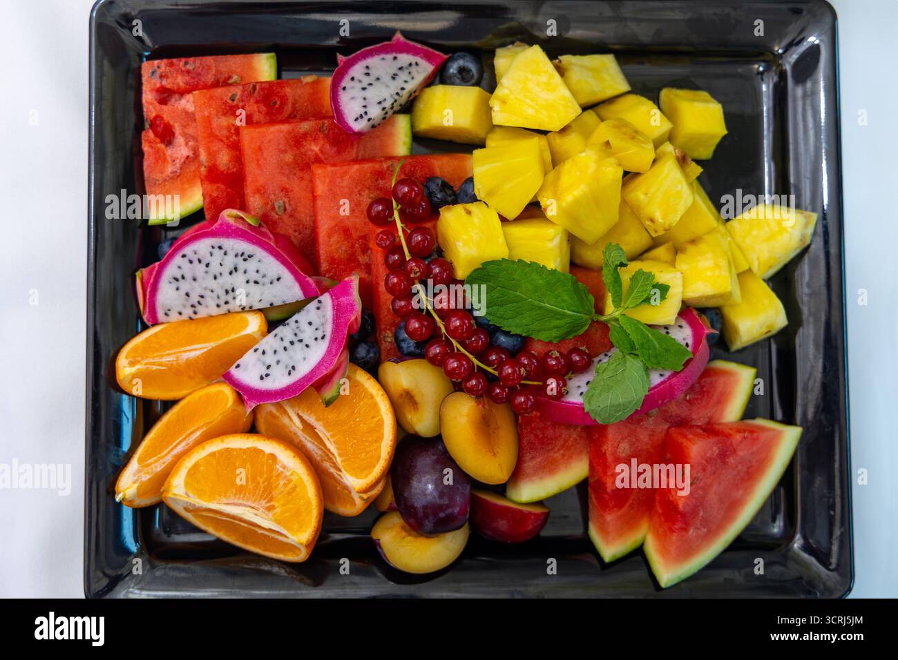 Farbenfrohe tropische Obstplatte mit Minzgarnitur. Helle und frische Auswahl an tropischen Früchten, darunter Wassermelone, Drachenfrüchte, Ananas Stockfoto
