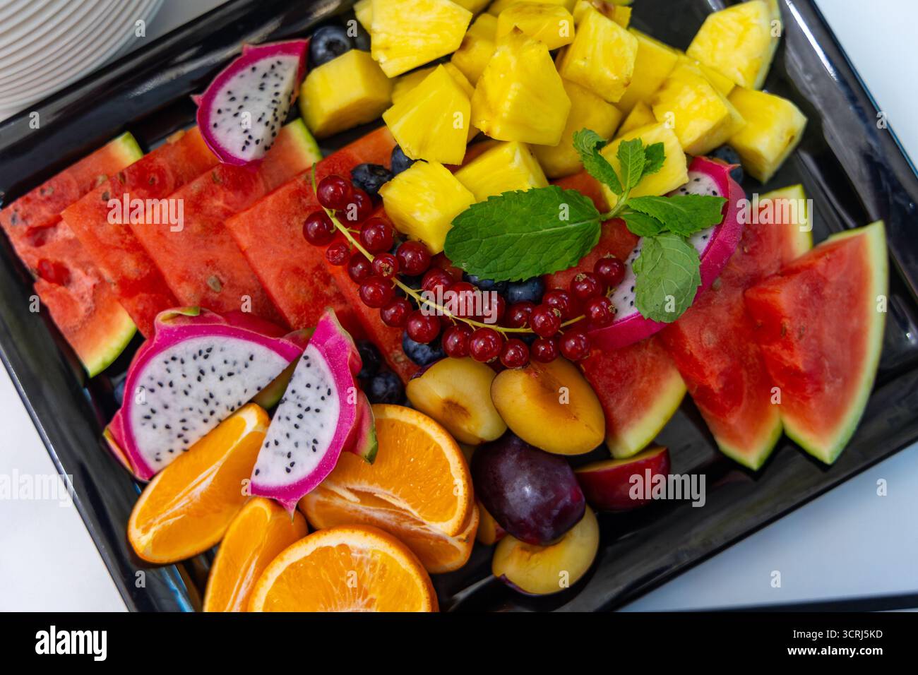 Frischer sommerlicher Obstteller mit tropischer Vielfalt. Blick von oben auf eine farbenfrohe Obstplatte mit Wassermelone, Ananas, Drachenfrucht und Orangen Stockfoto