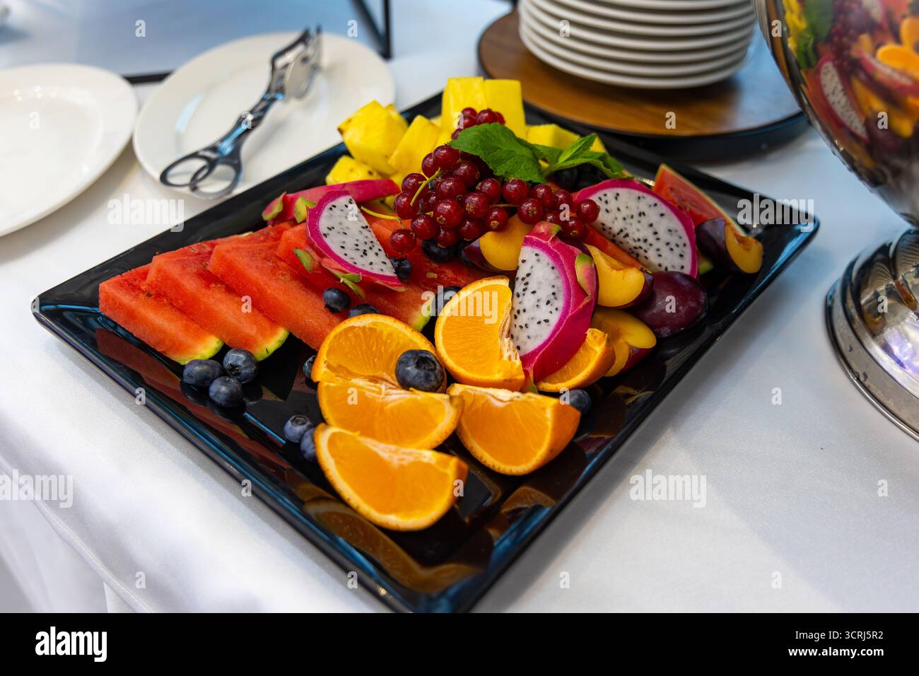 Tropische Obstplatte mit Wassermelonen und Drachenfrüchten. Farbenfrohe Obstarrangements auf einem schwarzen Tablett mit geschnittenen Wassermelonen, Drachenfrüchten und Orangen Stockfoto