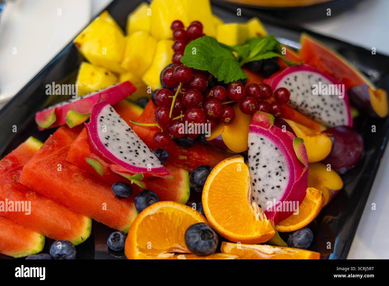 Lebendige tropische Obstplatte für Sommererfrischungen. Nahaufnahme einer farbenfrohen Obstplatte mit geschnittener Wassermelone, Drachenfrucht, Ananas, Orange Stockfoto