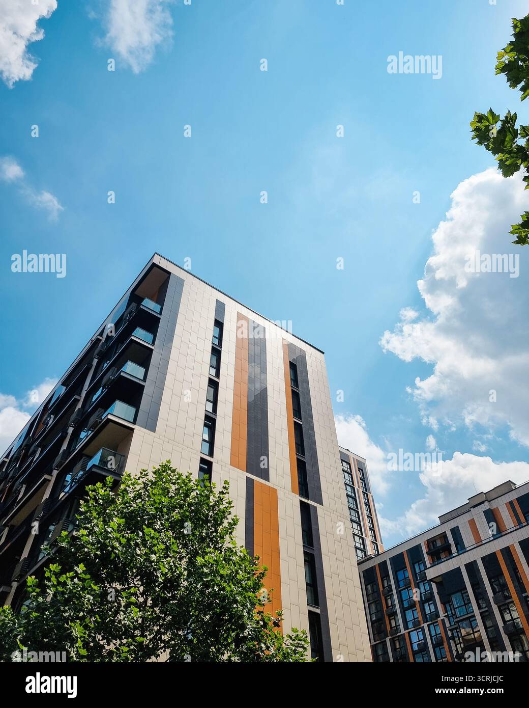 In einem modernen Wohnviertel in den Himmel blickend. Farbenfrohe Hochhäuser mit Fassaden, die mit grauen, orangen und beigen Streifen verziert sind. Stockfoto