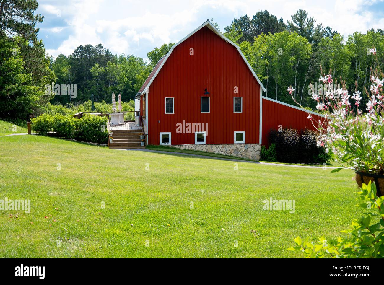 Schöne rote Scheune mit grünem Rasen, Blumen und Bäumen in ländlicher Umgebung in Minnesota. Stockfoto
