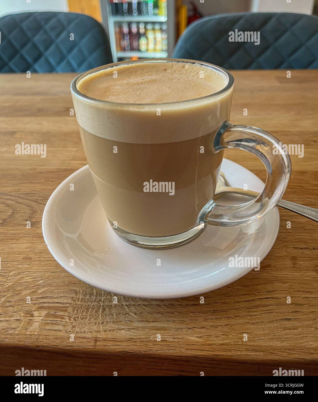 Glas Latte Tasse auf weißer Keramikplatte im gemütlichen Café - Smartphone-aufgenommenes Stockfoto