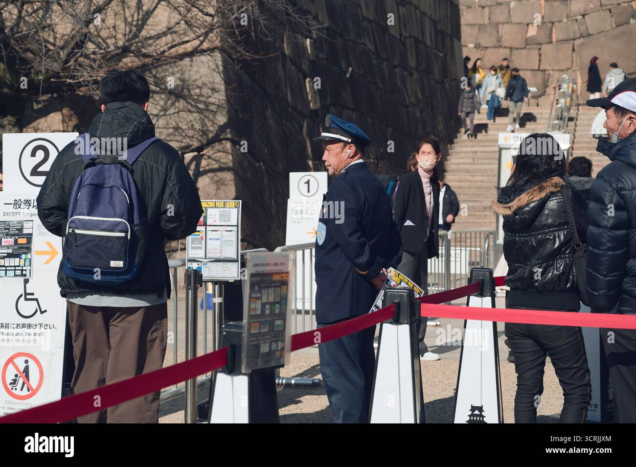 Der Sicherheitsbeamte überwacht die Besucher an der Ticketkontrolle, die zur Steintreppe des Schlosses Osaka führt Stockfoto