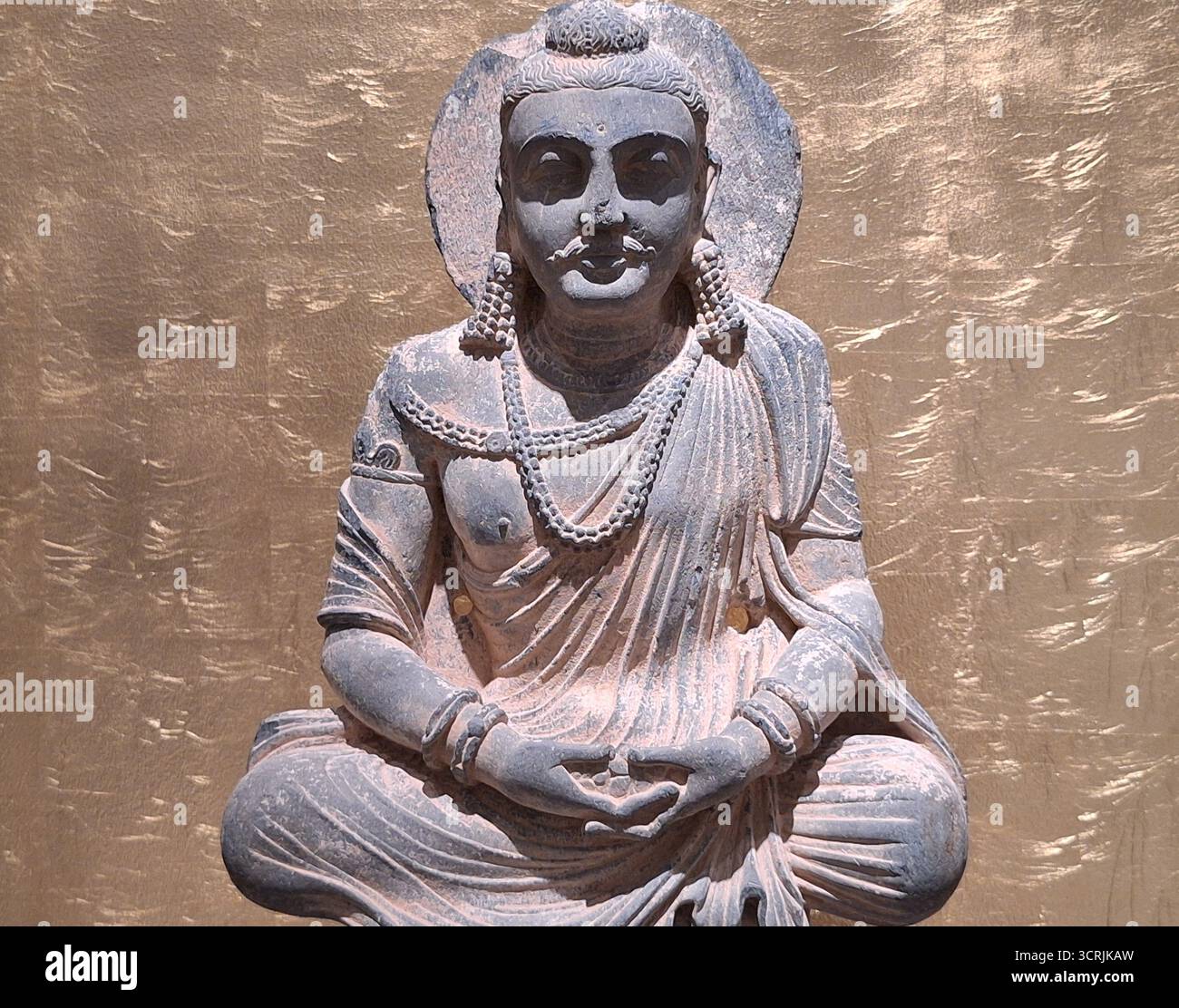 Buddhistische Meditationskunst: Nahaufnahme der meditierenden Bodhisattva-Statue vor einem kunstvollen goldenen Hintergrund in einem asiatischen Tempel Stockfoto