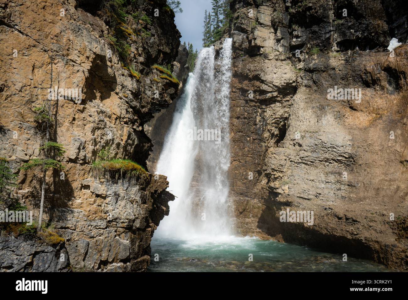 Der Wasserfall stürzt kraftvoll in eine felsige Schlucht mit türkisfarbenem Wasser. Stockfoto