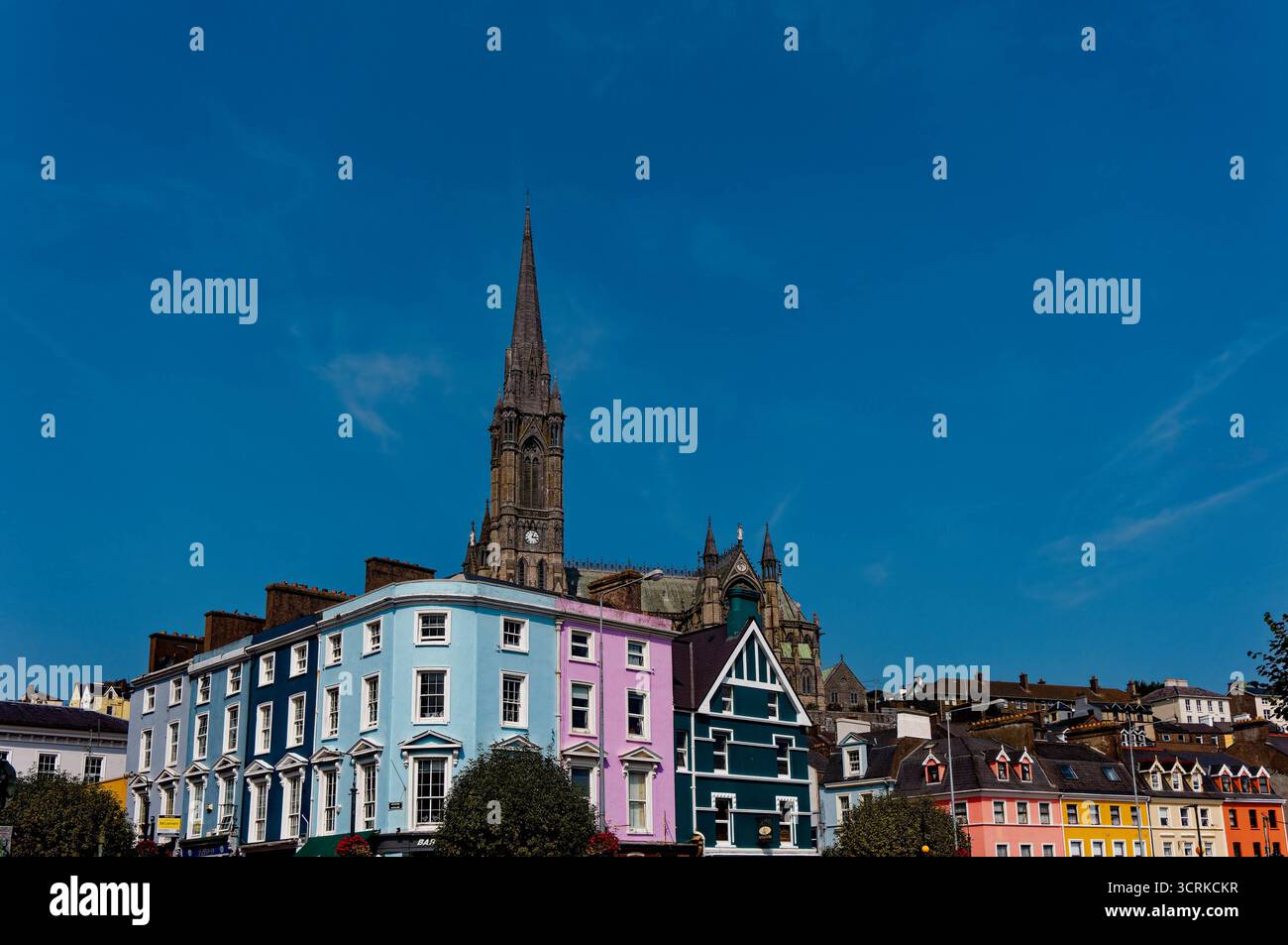 COBH, IRLAND - 15. August 2025: Die St. Colman's Cathedral erhebt sich über den farbenfrohen Geschäften und Pubs von Cobh und zieht Touristen an das bezaubernde Wasserfro der Stadt Stockfoto