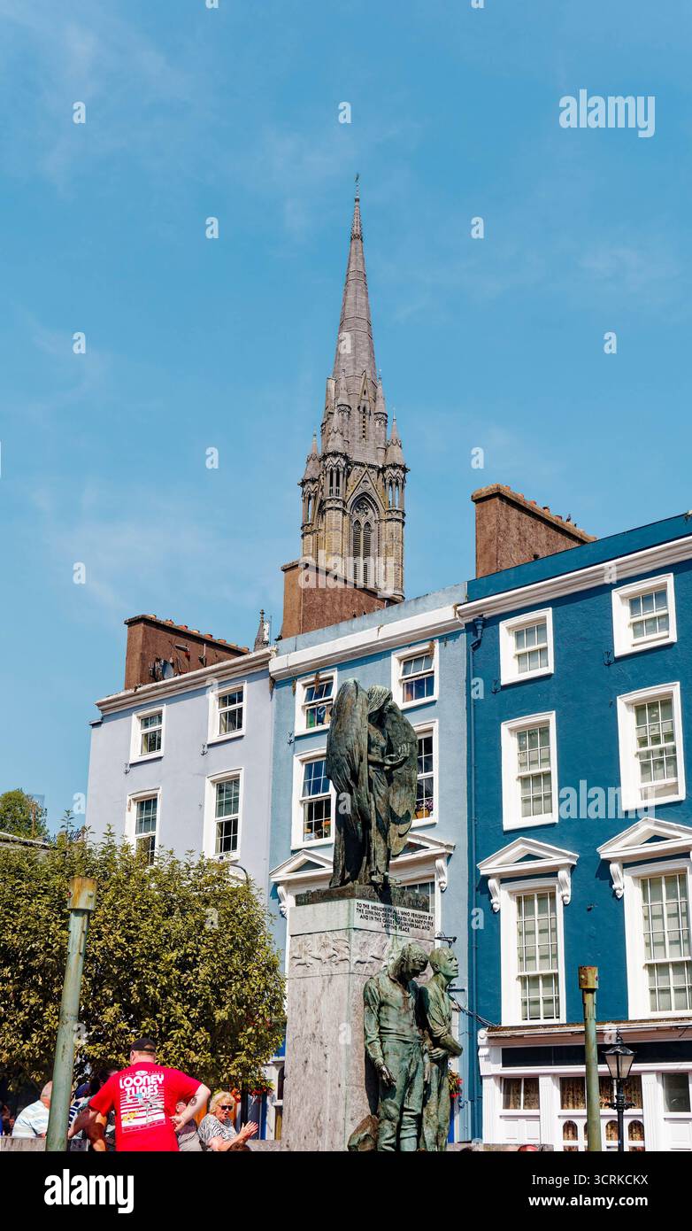 COBH, IRLAND - 15. August 2025: Die St. Colman's Cathedral erhebt sich über den farbenfrohen Geschäften und Pubs von Cobh und zieht Touristen an das bezaubernde Wasserfro der Stadt Stockfoto