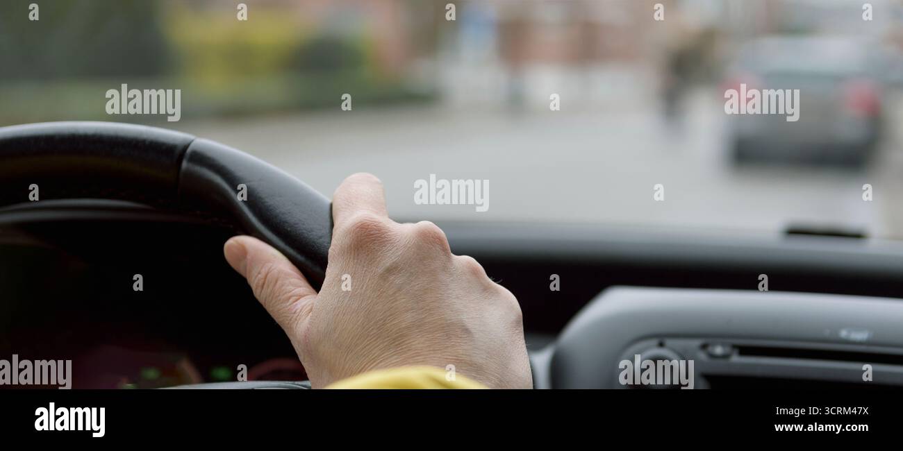 Die Hand einer Frau im Alter von 40-50 Jahren am Lenkrad eines Autos während der Fahrt Stockfoto