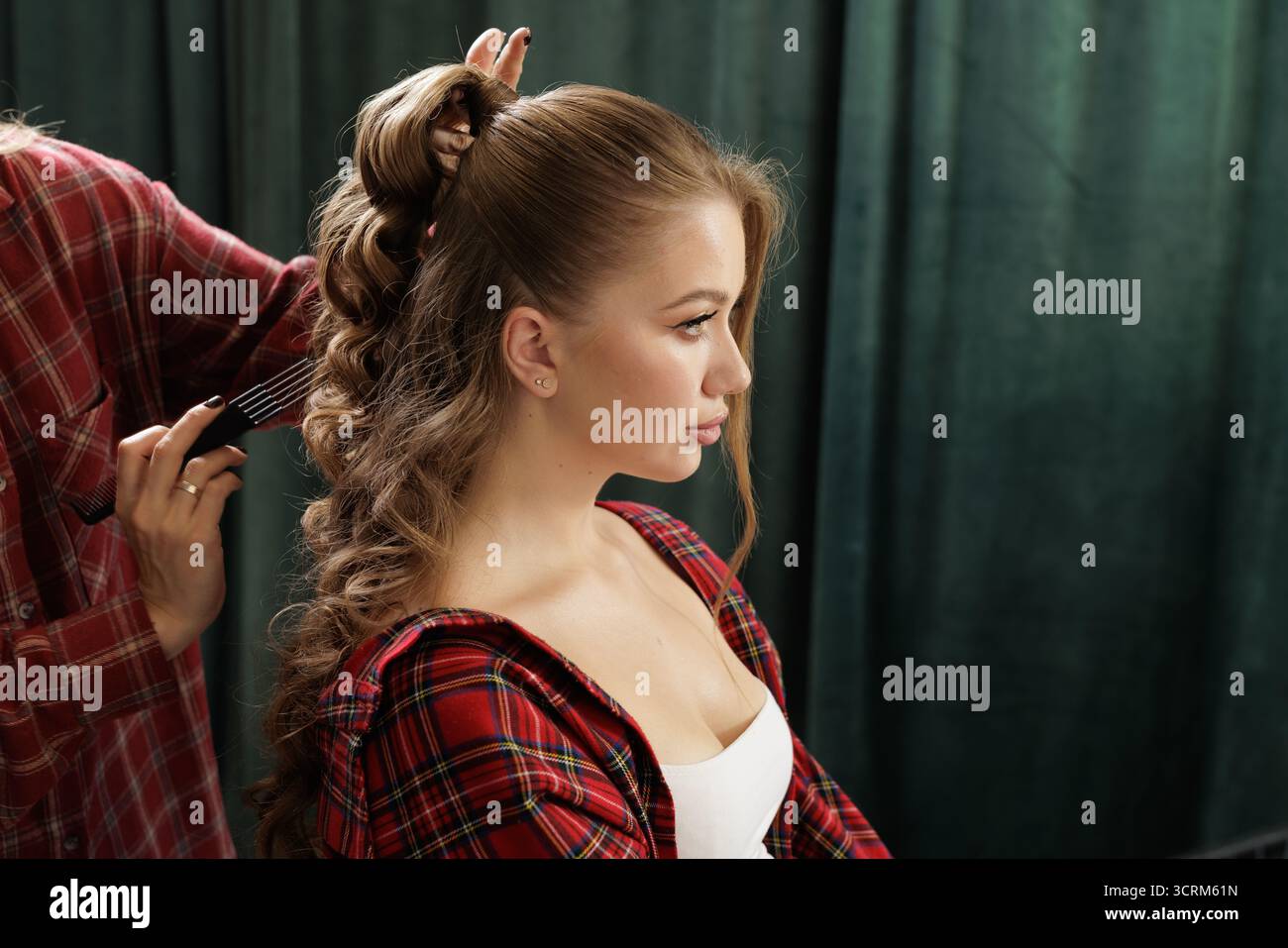 Seitenprofil eines Kunden als Stylist formt eine lockige Hochsteckfrisur mit abgeschnittenen Fäden und Kamm in einem Schönheitssalon, ideal für Haarpflege und Event-Inhalte. Stockfoto
