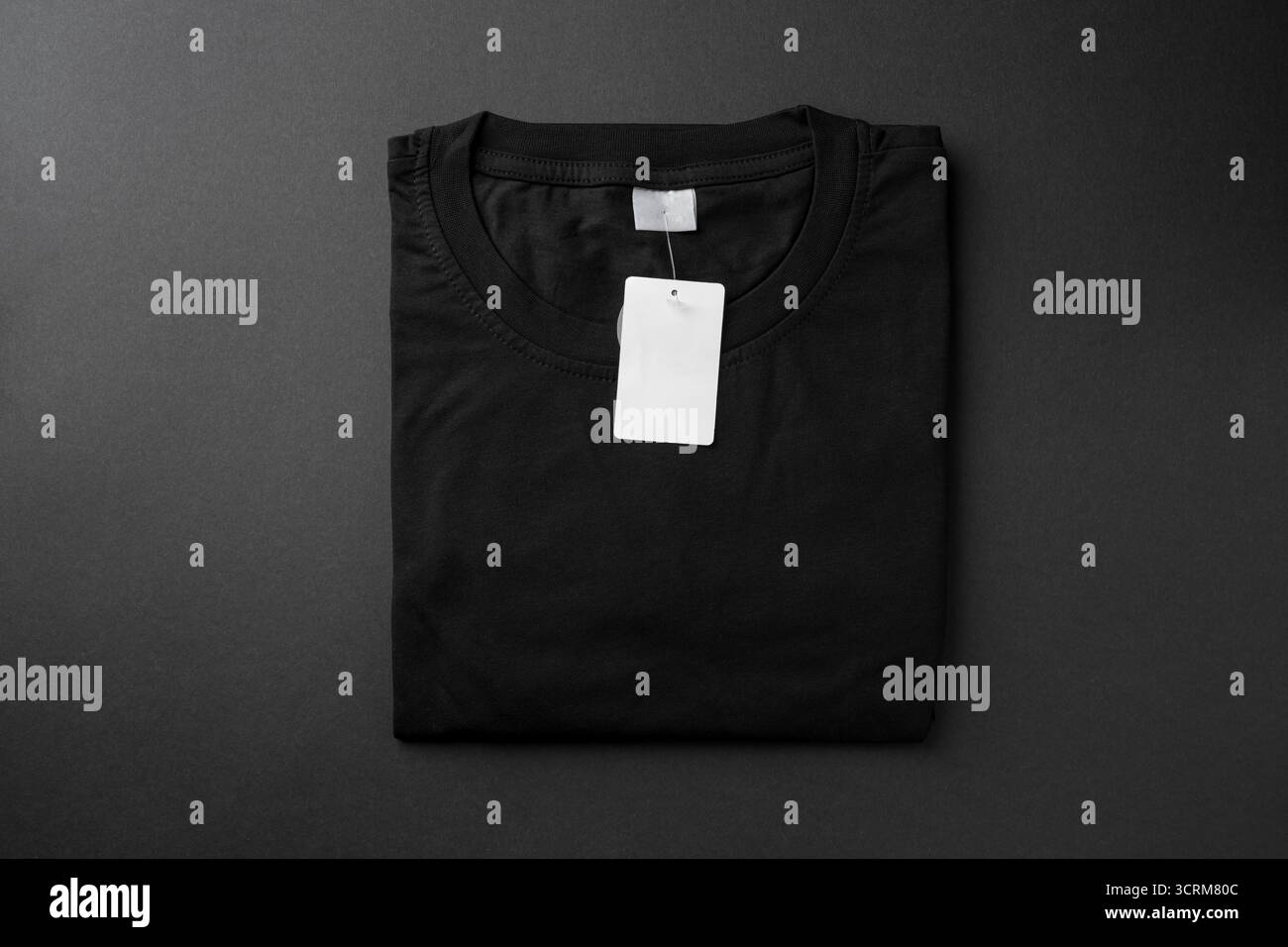Gefaltetes schwarzes T-Shirt mit leerem Papieranhänger auf dunklem Hintergrund Stockfoto