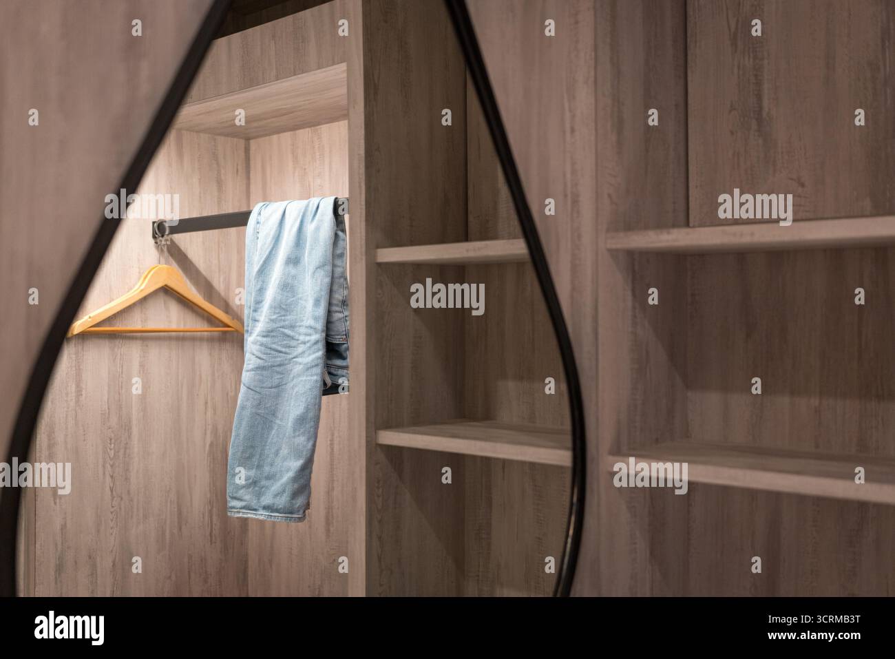 Offener Kleiderschrank mit langen Hosen und leeren Regalen. Stockfoto
