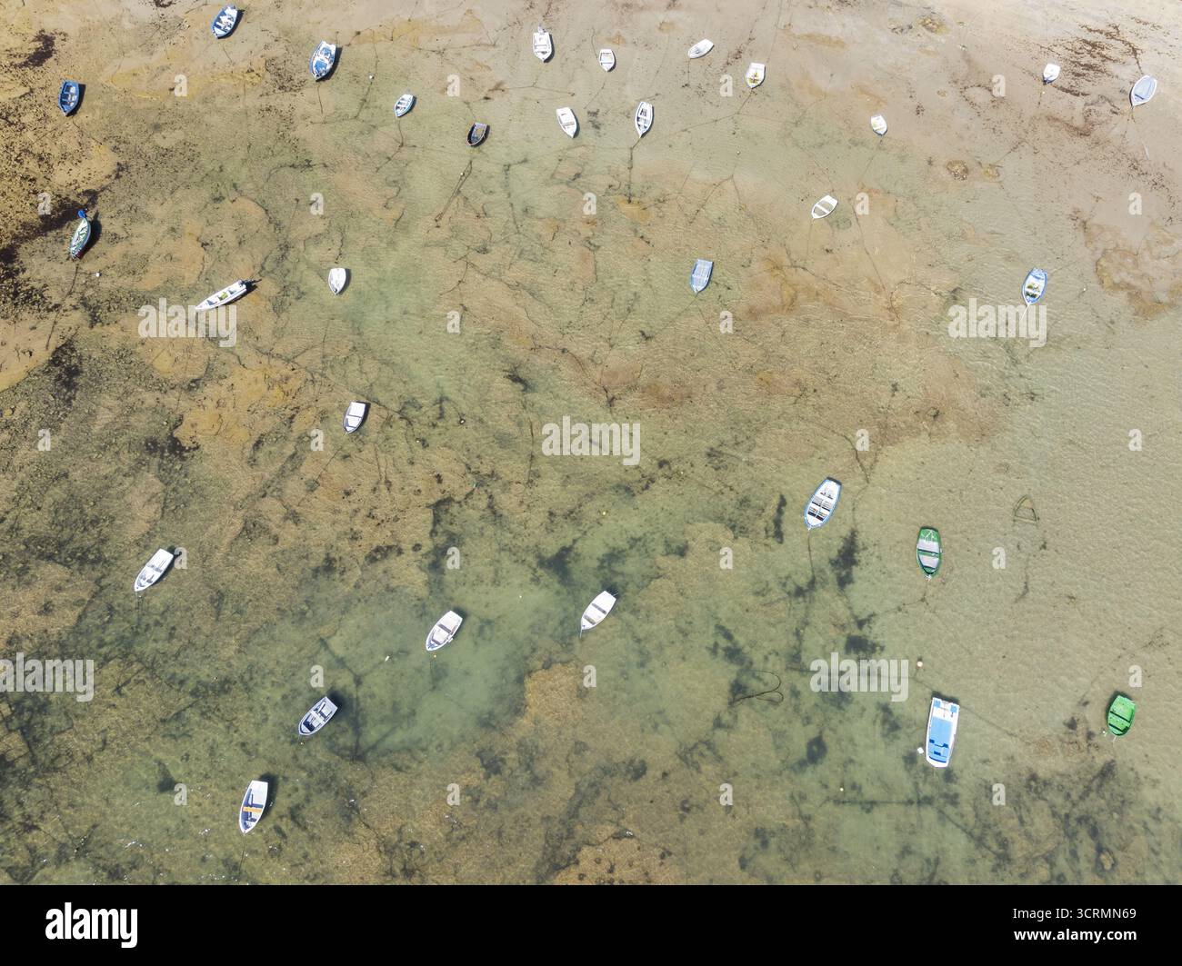 Aus der Vogelperspektive sehen Sie Boote, die über flaches türkisfarbenes Wasser verstreut sind und den Sandboden darunter enthüllen, wodurch ein Mosaik aus natürlichen Texturen entsteht, Cádiz, Andalusien, Spanien. Stockfoto