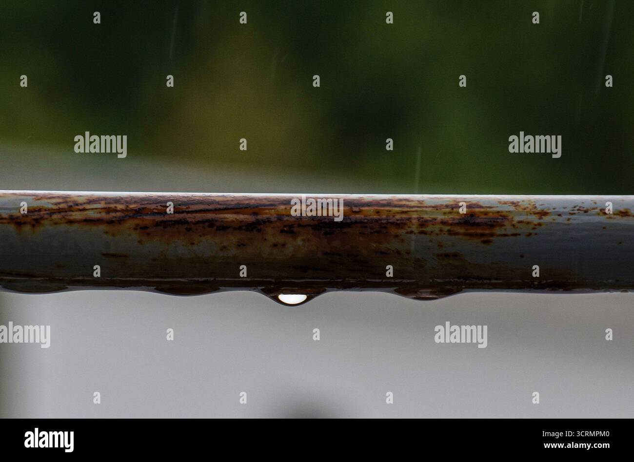 Ein graues Geländer mit Regentropfen und Rost, Blick auf die Terrasse mit geringer Tiefe für eine weiche, stimmungsvolle Kulisse. Stockfoto