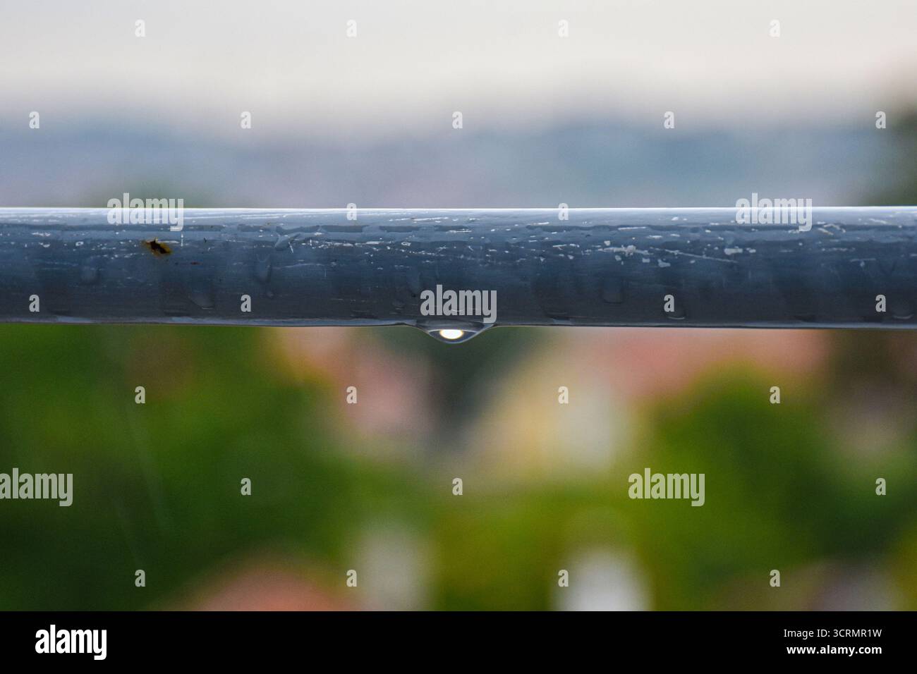 Eine feuchte, verwitterte Geländerbar auf der Terrasse mit scharfem Fokus, mit Regentröpfchen, die sich anklammern, und einer sanft verschwommenen Kulisse. Stockfoto