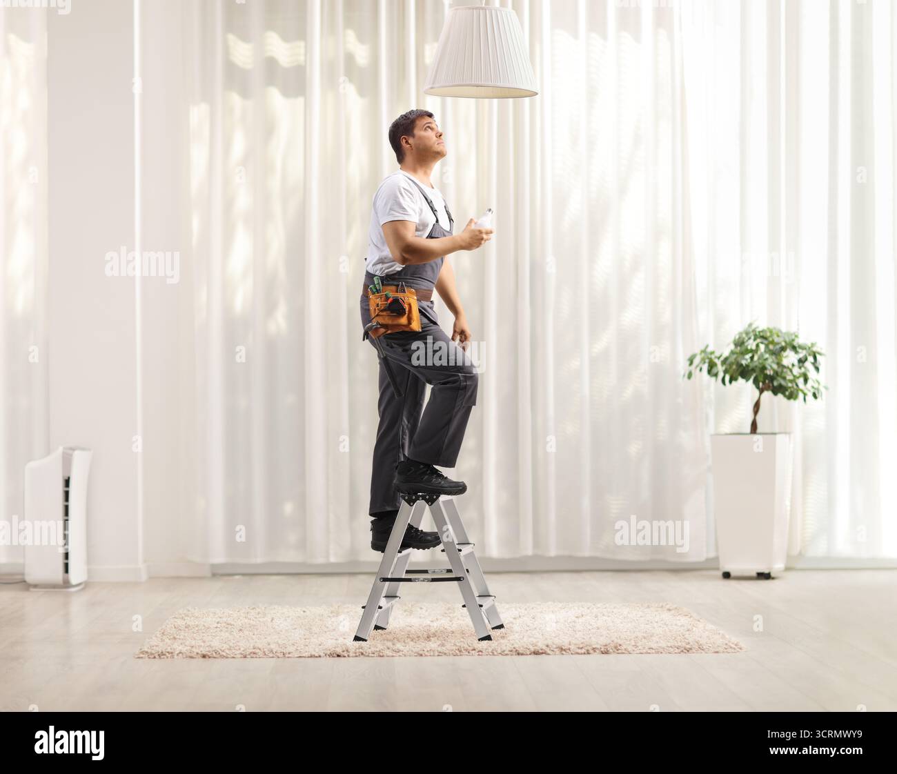 Arbeiter klettern auf eine kleine Leiter, um eine Pendelleuchte in einem Raum auszutauschen Stockfoto