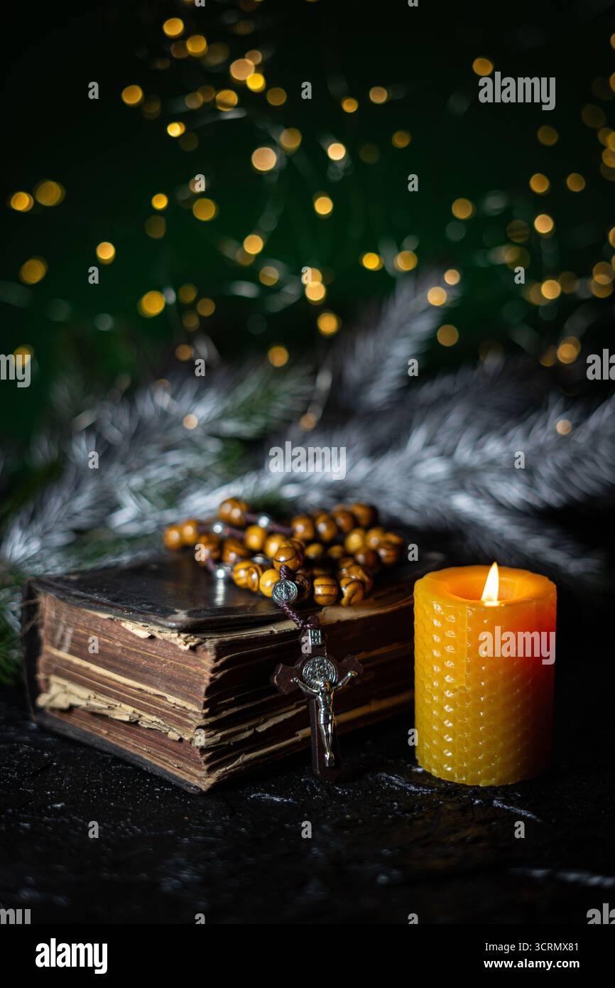 Gelbe Wachskerze, altes Gebetsbuch und Rosenkranzperlen auf grünem Hintergrund mit Bokeh-Lichtern. Adventskonzept. Stockfoto