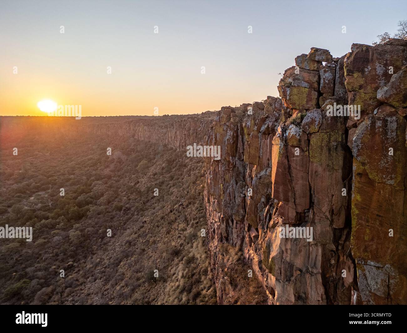 Panoramablick bei Sonnenuntergang auf rote Sandsteinklippen und Steilhänge des Waterberg Plateaus über Buschwald, Namibia, südliches Afrika. Stockfoto