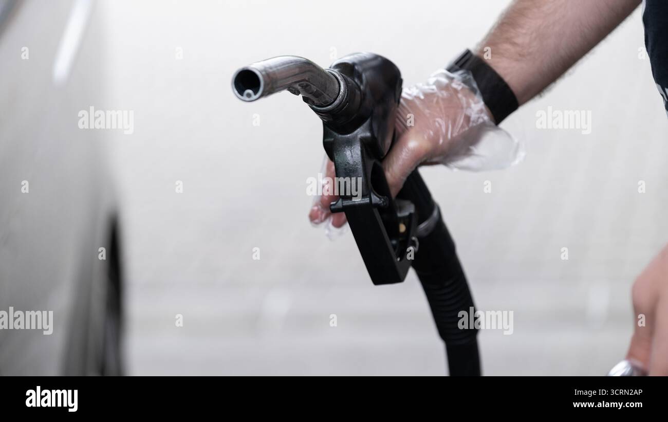 Mann betankt ein Fahrzeug mit Diesel an einer Tankstelle. Die Hand trägt einen Einweghandschuh zur Hygiene. Geeignet für die Veranschaulichung von Themen zu TRANS Stockfoto