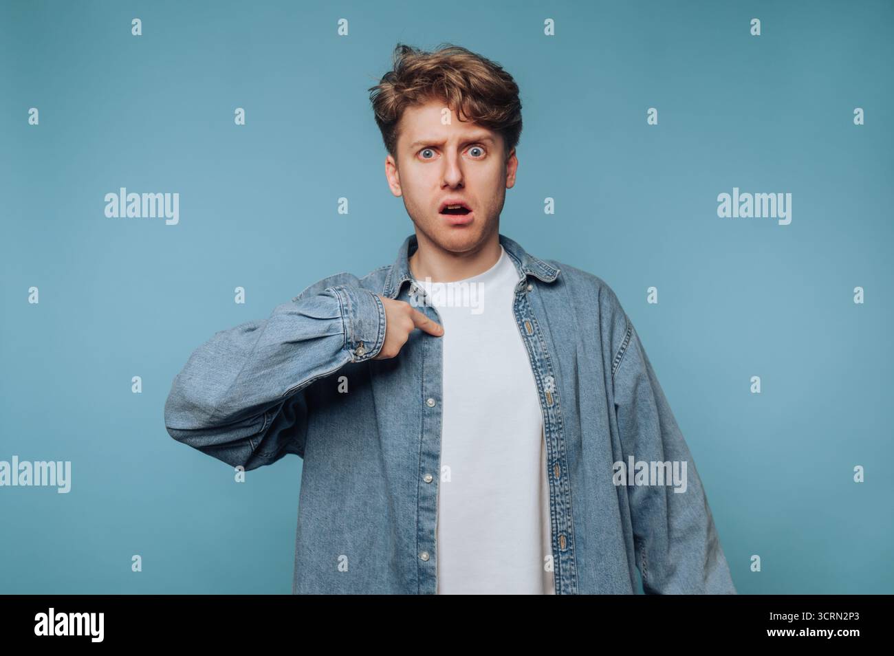 Junger Mann mit einem schockierten Ausdruck in einem lässigen Outfit vor blauem Hintergrund Stockfoto