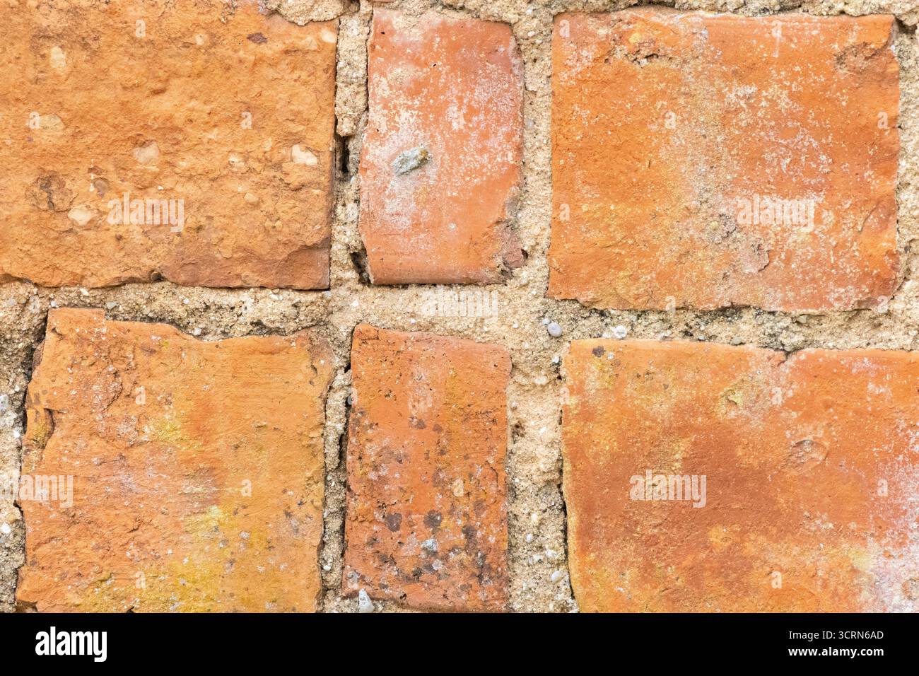 Orangefarbene Wandoberfläche aus Ziegelstein mit sichtbarem Mörtel und Alterungsspuren für einen strukturierten Hintergrund Stockfoto
