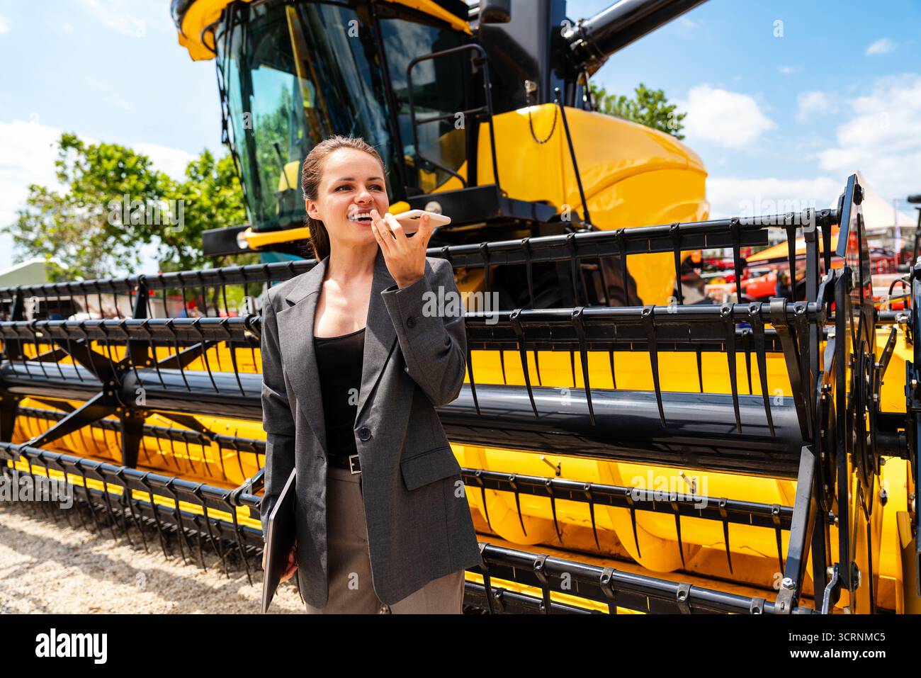 Moderne Landwirtschaftsfrau, die Sprachnachrichten von Mähdreschern im Händlerbetrieb auf dem Smartphone aufnimmt Stockfoto