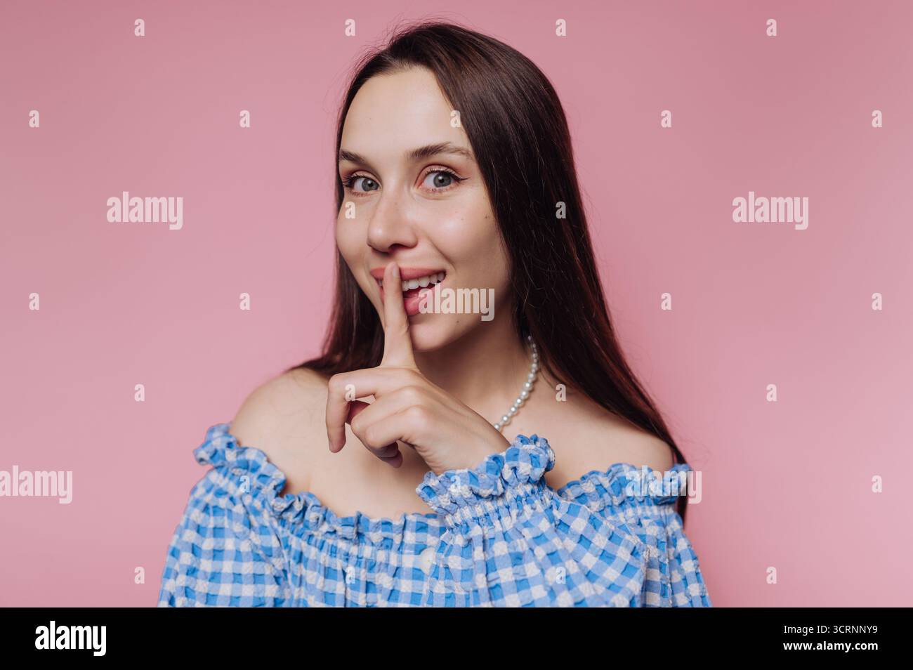 Frau in blau kariertem Off-Shoulder-Top, die eine Shushing-Geste macht. Stockfoto