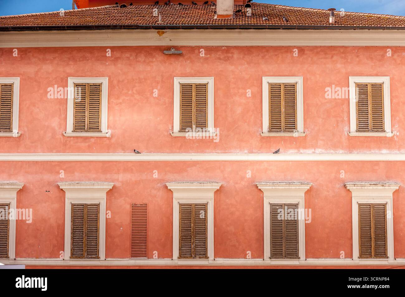 Farbenfrohe pinkfarbene Fassade mit Holzläden in Foligno, Umbrien, Italien, mit traditioneller italienischer Architektur und mediterranem Charme Stockfoto