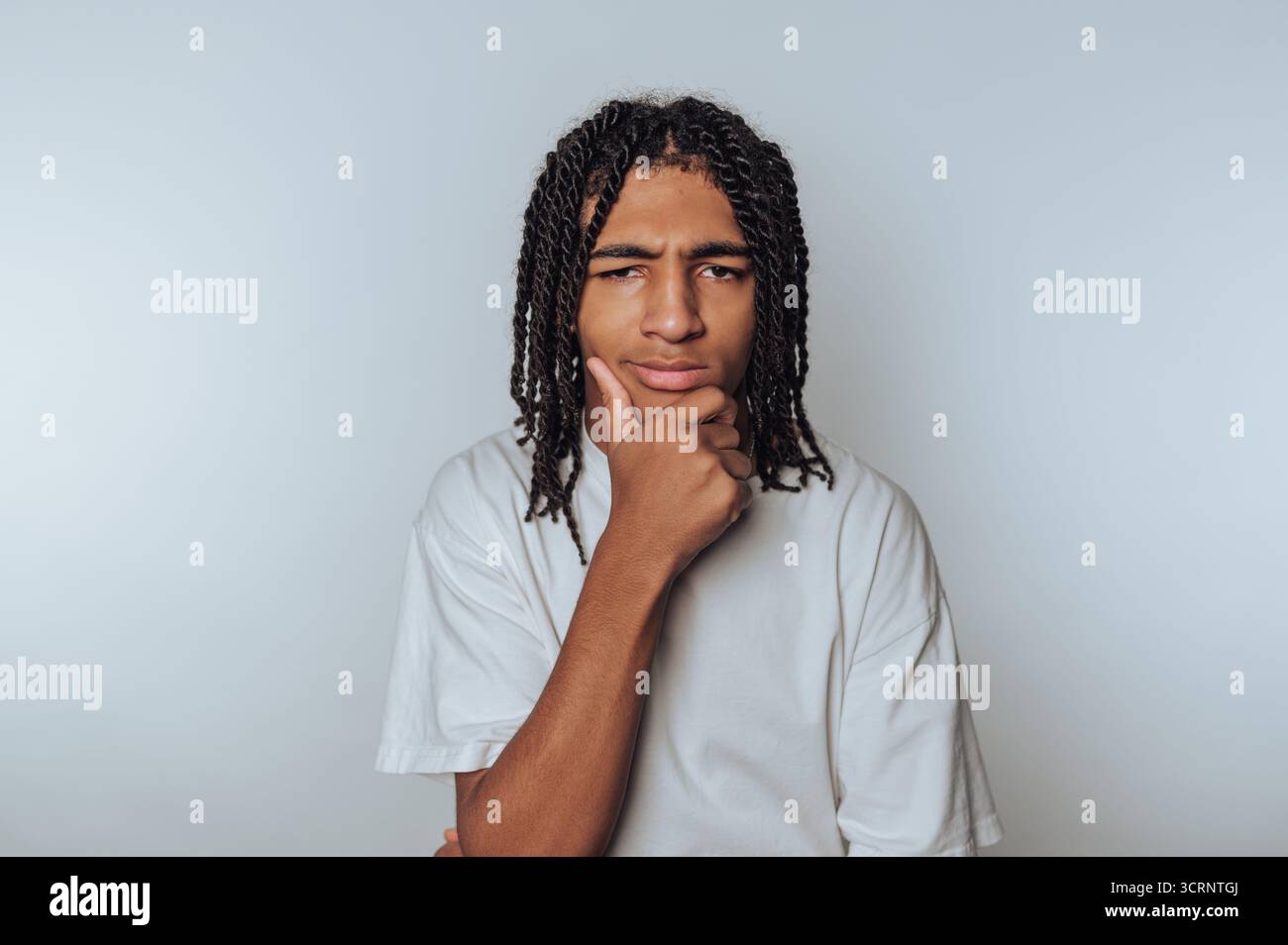 Porträt eines jungen Mannes mit einem nachdenklichen Ausdruck, der sein Kinn auf seiner Hand auflegt, was auf einen hellen Hintergrund hinweist Stockfoto