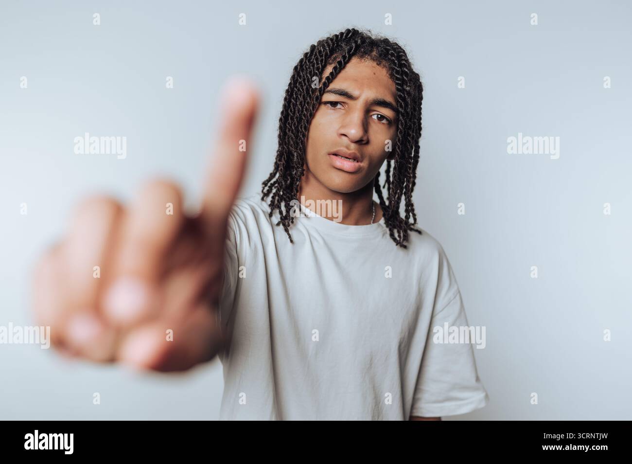 Porträt eines jungen Mannes mit Dreadlocks hebt seinen Finger, während er nachdenklich wirkt und einen Moment der Nachdenklichkeit auf hellem Hintergrund vermittelt Stockfoto