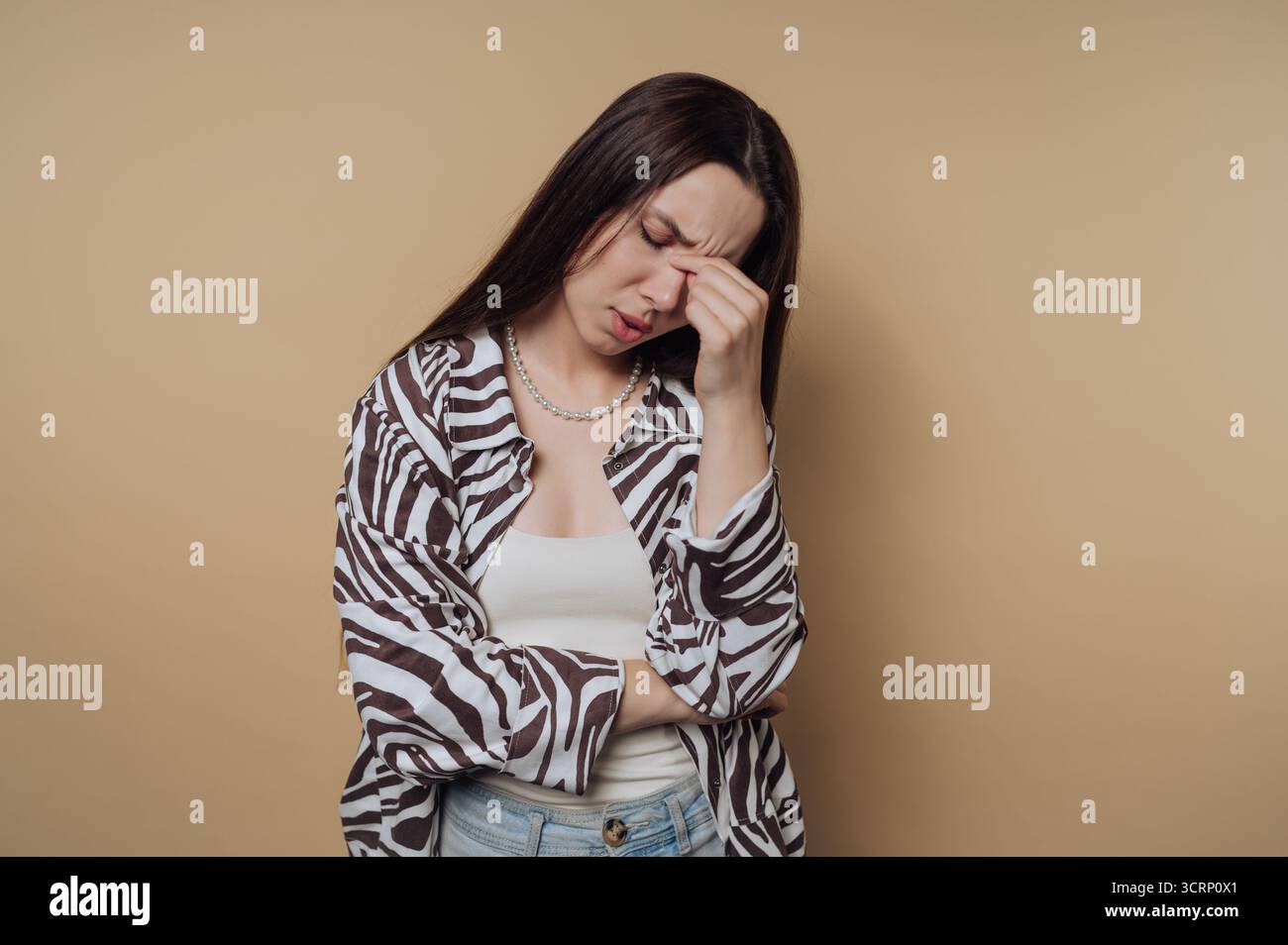 Eine junge Frau zeigt ihre Frustration, indem sie ihre Hand auf ihre Stirn legt. Sie trägt einen gestreiften Schal über einem weißen Oberteil und scheint dabei zu sein Stockfoto